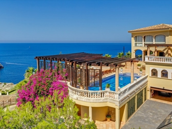 An image of a traditional sea view villa in Port Andratx, showcasing classic Mediterranean architecture with terracotta roofs, stone facades, and elegant arches. The villa is surrounded by lush gardens and offers breathtaking views of the Mediterranean Sea. Inside, the home combines rustic charm with modern comforts, featuring spacious rooms with natural light, cozy living areas, and stylish décor. The outdoor space includes a private pool, large terrace, and shaded seating areas, ideal for enjoying the stunning coastal landscape.