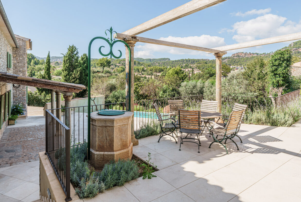 An image of a newly built home with charm in Es Capdella, featuring a harmonious blend of modern design and traditional Mediterranean style. The house boasts a warm and inviting atmosphere with natural materials such as stone and wood, complemented by sleek, contemporary finishes. Large windows allow for plenty of natural light, while the spacious open-plan interiors offer comfort and elegance. The outdoor area includes beautifully landscaped gardens, a private pool, and a large terrace, perfect for enjoying the serene surroundings of this peaceful village