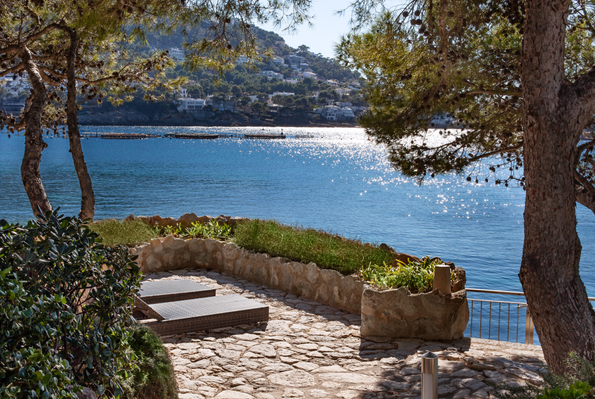 An image of a stunning frontline home in Port Andratx, featuring direct access to the water and a private boathouse. The home is designed with sleek, modern architecture, offering expansive windows that provide breathtaking views of the harbor and Mediterranean Sea. The boathouse is ideally located on the property, allowing for easy docking and access to water activities. The beautifully landscaped outdoor space includes a private terrace, pool, and lounge areas, creating an exclusive, luxurious waterfront retreat.