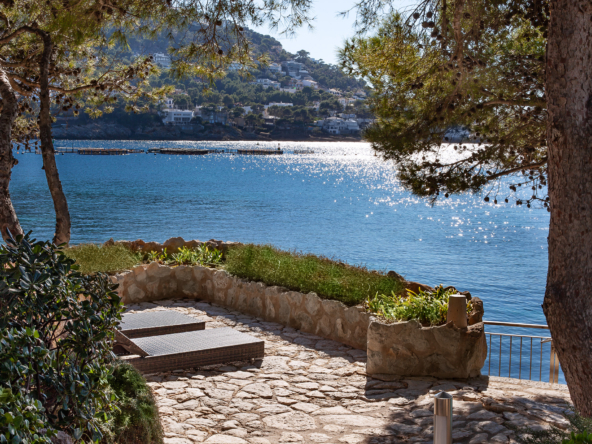 An image of a stunning frontline home in Port Andratx, featuring direct access to the water and a private boathouse. The home is designed with sleek, modern architecture, offering expansive windows that provide breathtaking views of the harbor and Mediterranean Sea. The boathouse is ideally located on the property, allowing for easy docking and access to water activities. The beautifully landscaped outdoor space includes a private terrace, pool, and lounge areas, creating an exclusive, luxurious waterfront retreat.