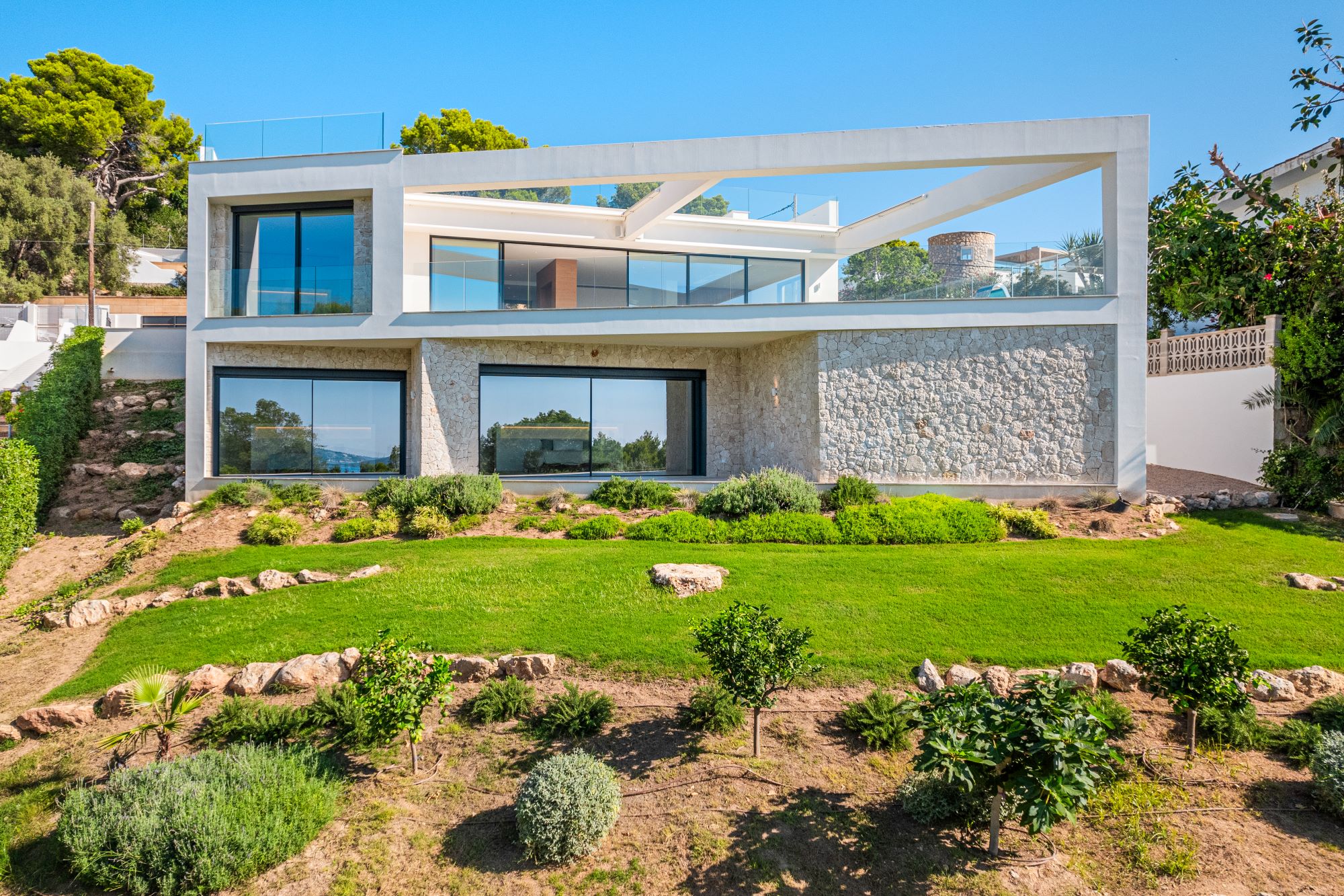 "An image of a sleek designer home with breathtaking views. The house features contemporary architecture with clean lines, large glass windows, and a minimalist aesthetic. The interior opens seamlessly to an outdoor terrace, where stylish furnishings invite relaxation. Beyond, panoramic views of rolling hills, a sparkling coastline, or a vibrant cityscape stretch into the distance, creating a harmonious blend of luxury and natural beauty."