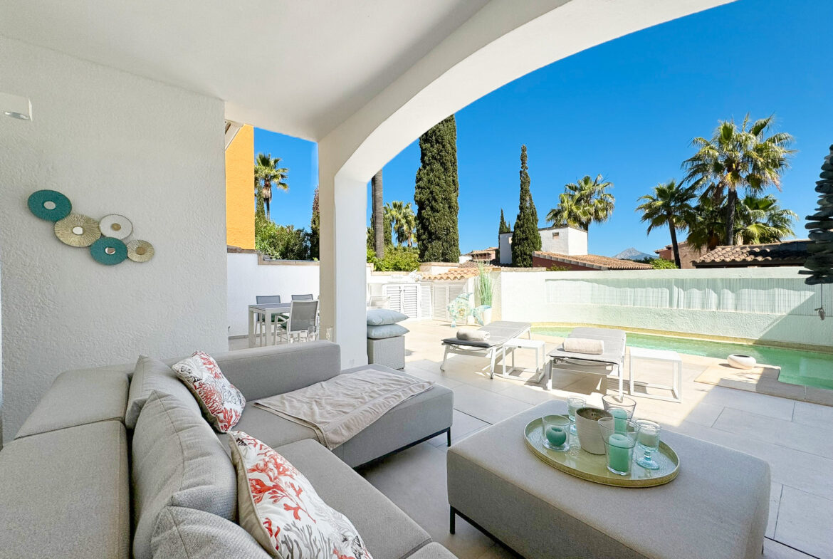 An image of a beautiful Torre-style house in Abubillas, showcasing its traditional Mediterranean charm. The home features rustic stone walls, arched doorways, and a signature tower element that adds character to its design. Surrounded by a lush garden filled with vibrant flowers and mature trees, the house exudes warmth and elegance. The sunlit setting highlights its unique architecture, blending timeless appeal with natural beauty.