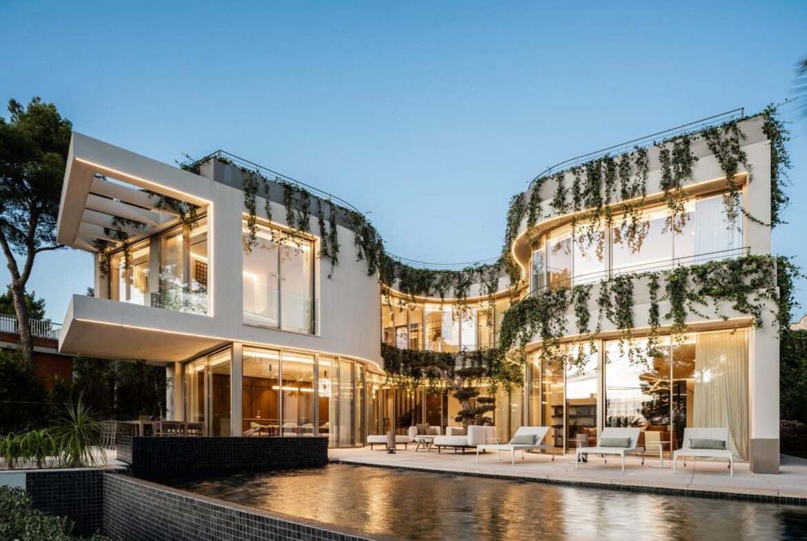 An image of a stunning architectural masterpiece located near the beach. The structure features bold, contemporary design with clean lines, expansive glass panels, and unique geometric elements. Surrounded by a meticulously landscaped garden, the home seamlessly blends into its coastal environment. In the background, the golden sands and azure waves of the nearby beach enhance the property's allure, reflecting its exclusive and sophisticated character.