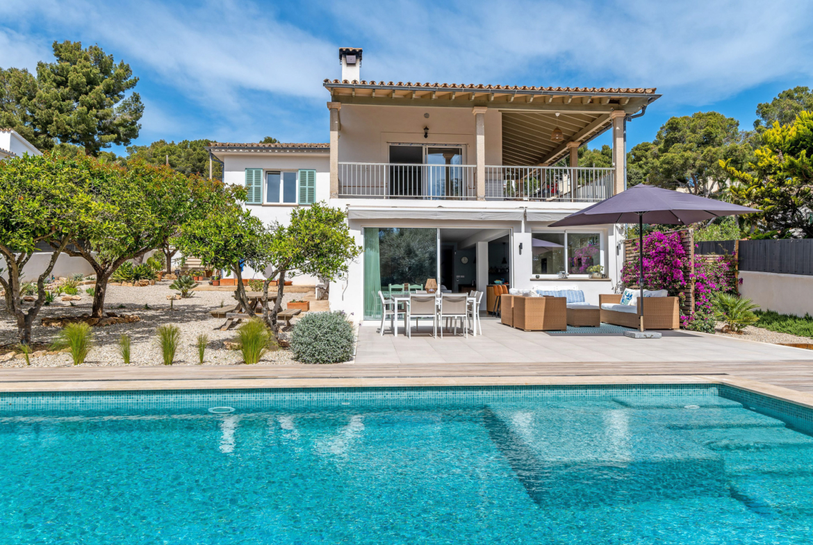 An image of a traditional house that has been beautifully renovated, featuring a charming blend of classic and modern architecture. The house is surrounded by a well-maintained garden with lush greenery and vibrant flowers. In the foreground, a sparkling blue swimming pool reflects the sunlight, adding a touch of luxury to the serene outdoor setting.